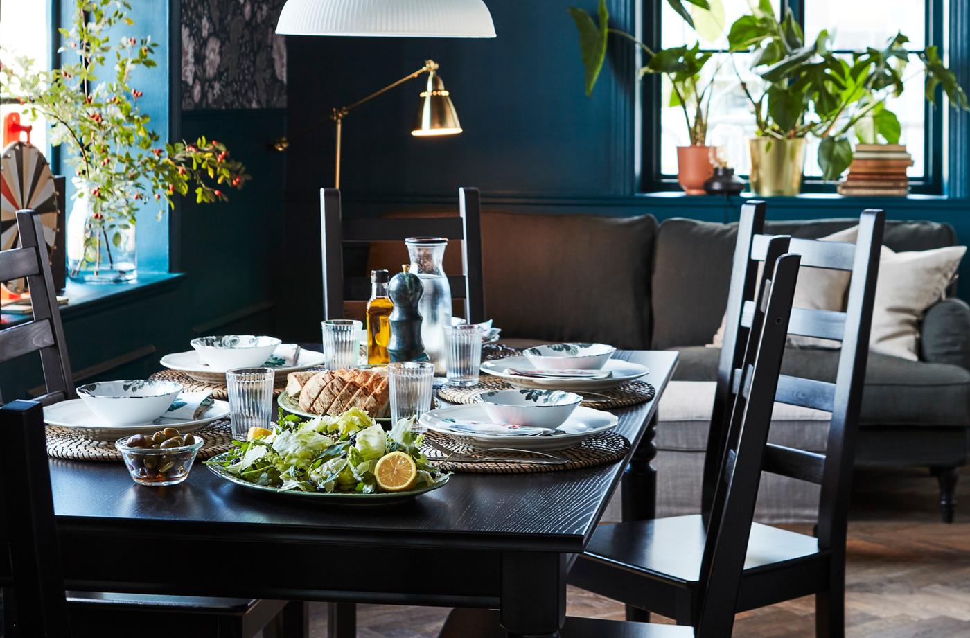 Dark dining room with black dining table and chairs. Table is set with white dishes and round placemats.