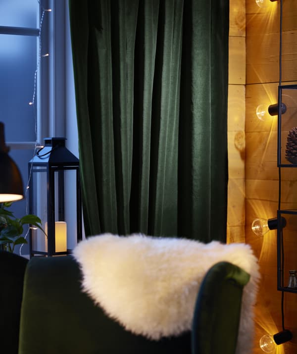 Dark green cotton SANELA curtains are pulled aside to reveal a window adorned with string lights