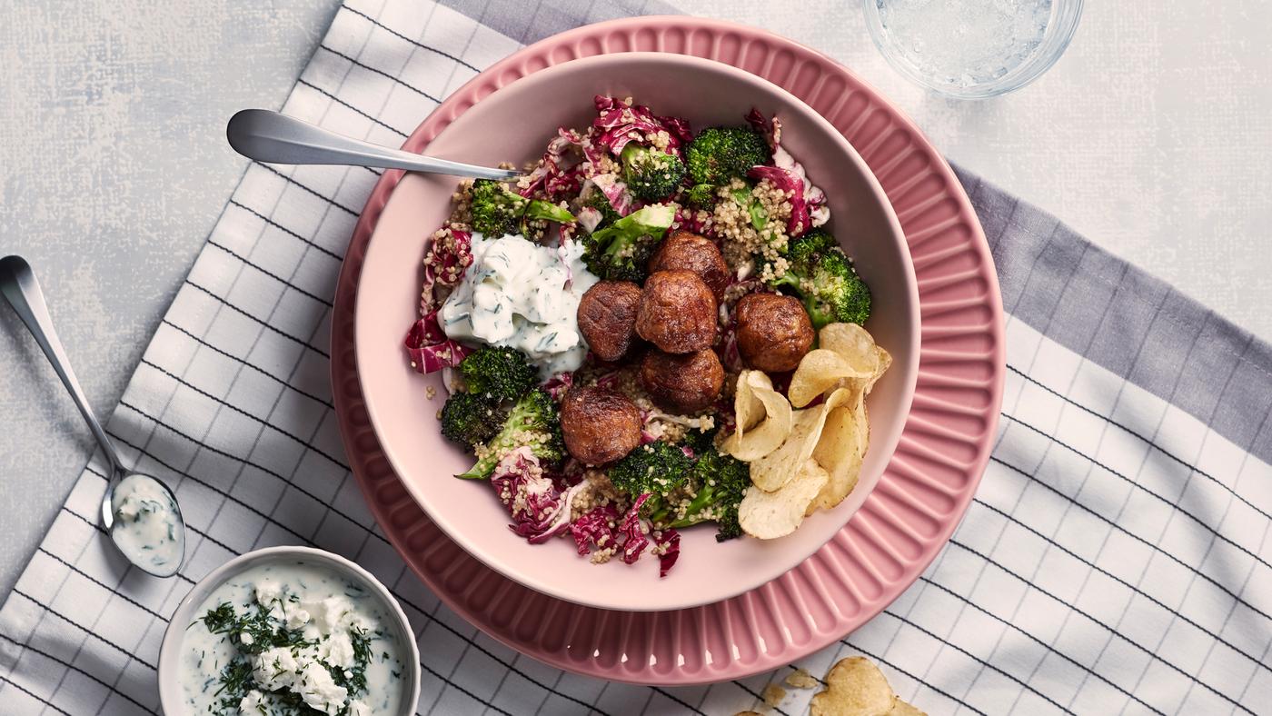 De la salade de quinoa avec boulettes à base de végétaux dans un bol blanc sur une assiette rose, laquelle est posée sur un torchon à carreaux blanc et gris.
