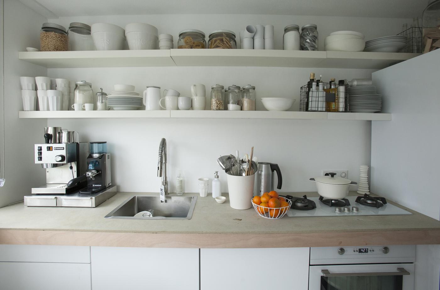De longues tablettes aux murs au-dessus de l’évier de cuisine et du plan de travail servent de rangements ouverts.