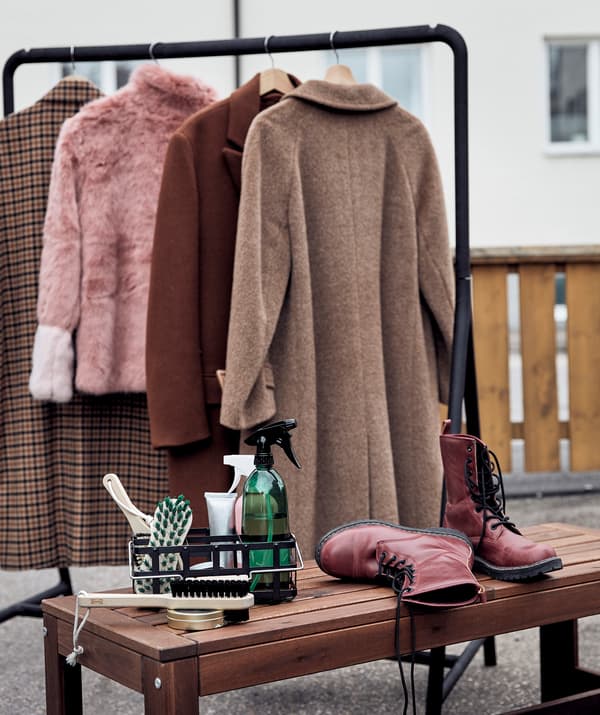 Décor d’extérieur avec une tringle à vêtements TURBO sur laquelle sont suspendus des vêtements d’hiver à côté d’un banc avec une paire de chaussures et un nécessaire de nettoyage.