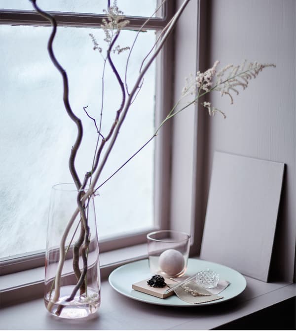 Décoration de fenêtre réalisée avec des branches disposées dans un grand vase.