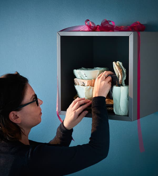 Décoratrice d'intérieur en train de disposer les pièces de vaisselles emballées sur une étagère.