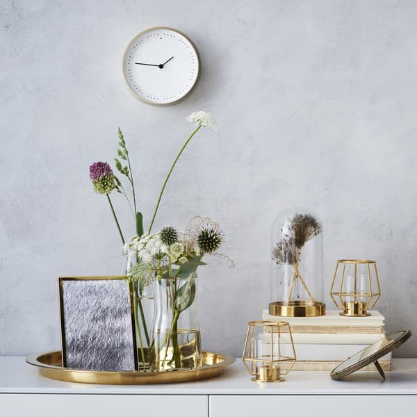 Des accessoires déco métalliques et un arrangement floral sur un meuble blanc.
