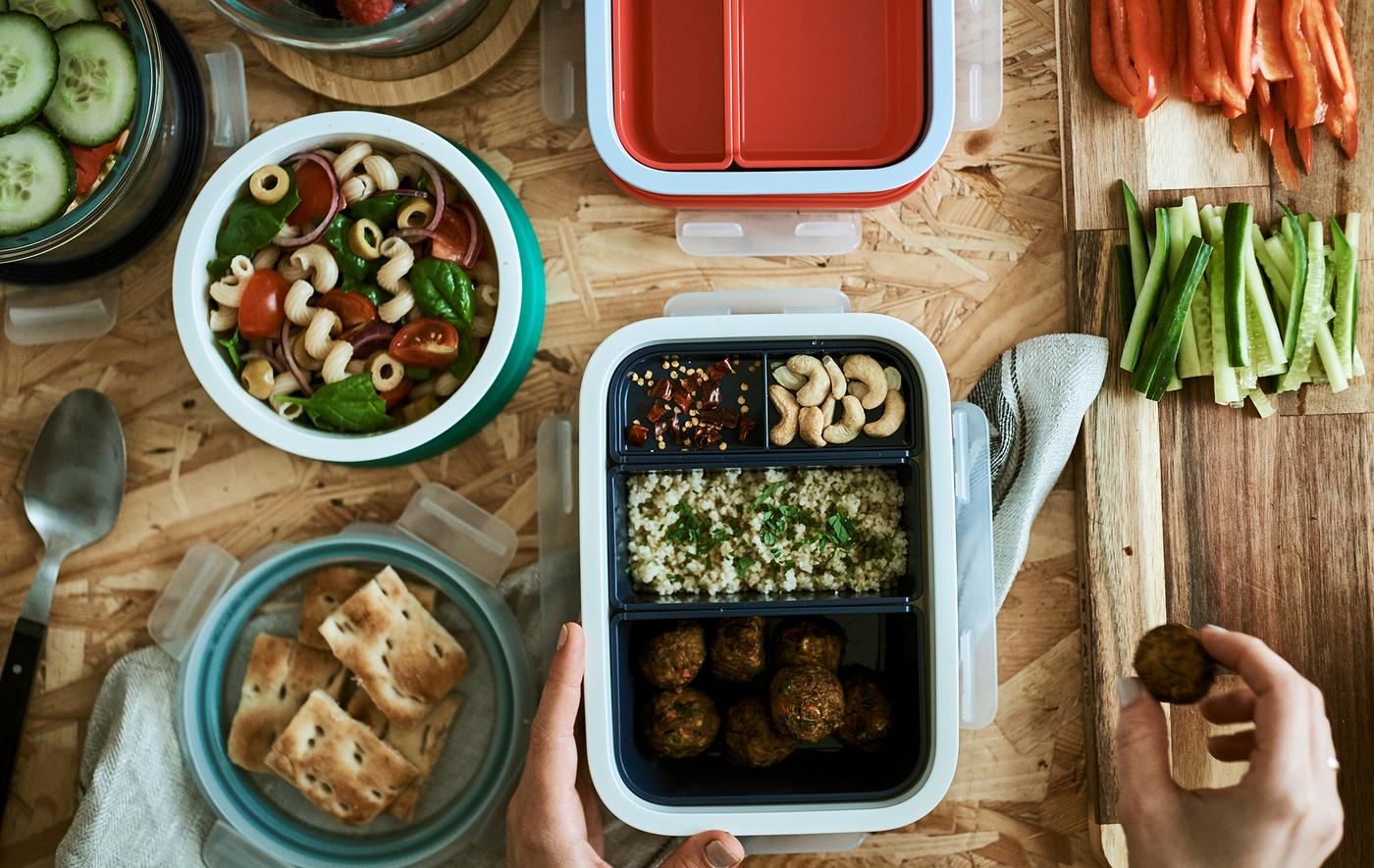 Des aliments emballés dans des boîtes à déjeuner. L’une d'entre elles a des compartiments avec différents aliments, un récipient en plastique rond contient de la salade de pâtes.