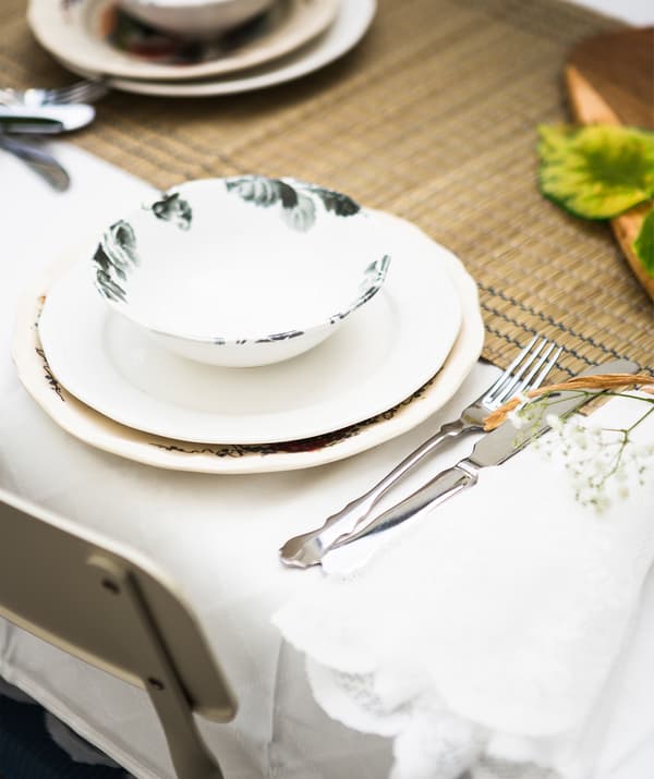 Des assiettes et des couverts disposés sur un chemin de table en jonc de mer et une nappe blanche.