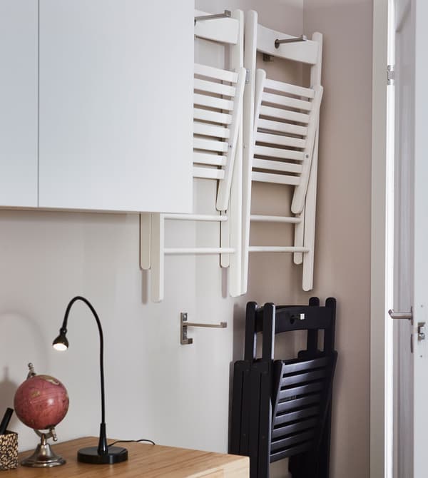 Des chaises pliantes de réserve sont accrochées au mur, derrière la porte du séjour.