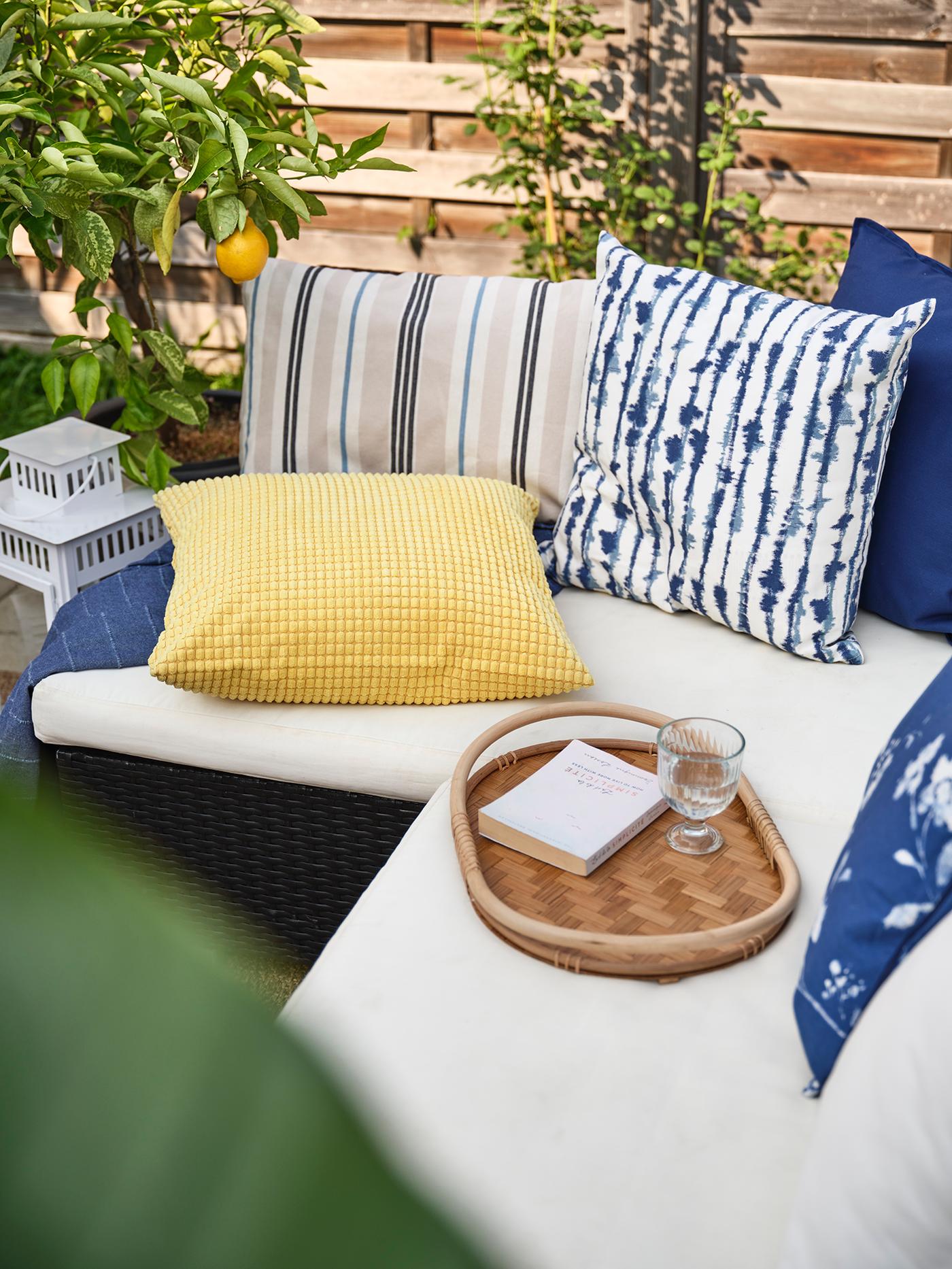 Des coussins bleus et jaunes posés sur un canapé d'extérieur beige.