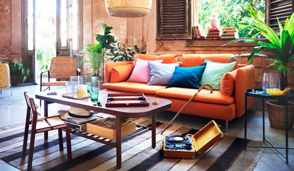 Des coussins colorés posés sur un canapé SÖDERHAMN orange dans un salon. Sur une table basse, des boissons et un jeu de société.
