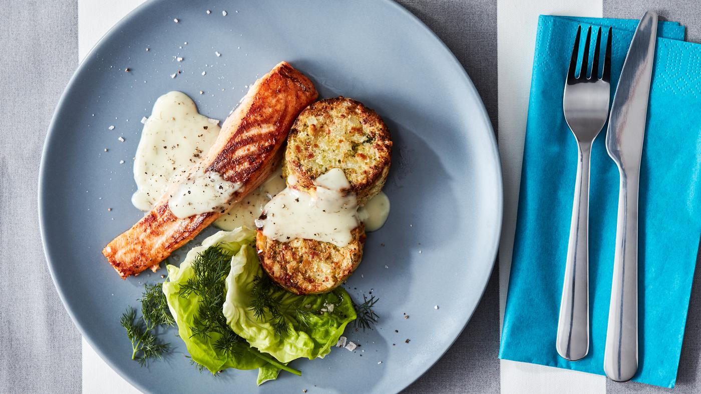 Des couverts DRAGON et une assiette gris-bleu avec filet de saumon SJÖRAPPORT, salade, sauce et médaillons de légumes GRÖNSAKSKAKA.