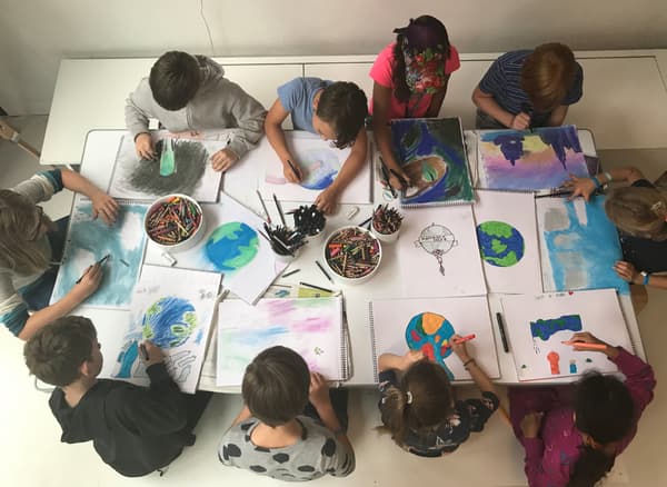 Des enfants assis autour d’une table font des dessins de la Terre.