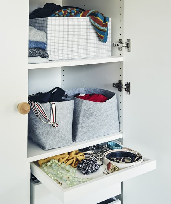 Des étagères d'armoire remplies de paniers, de boîtes et de vêtements pliés, ainsi qu’un tiroir d’accessoires.