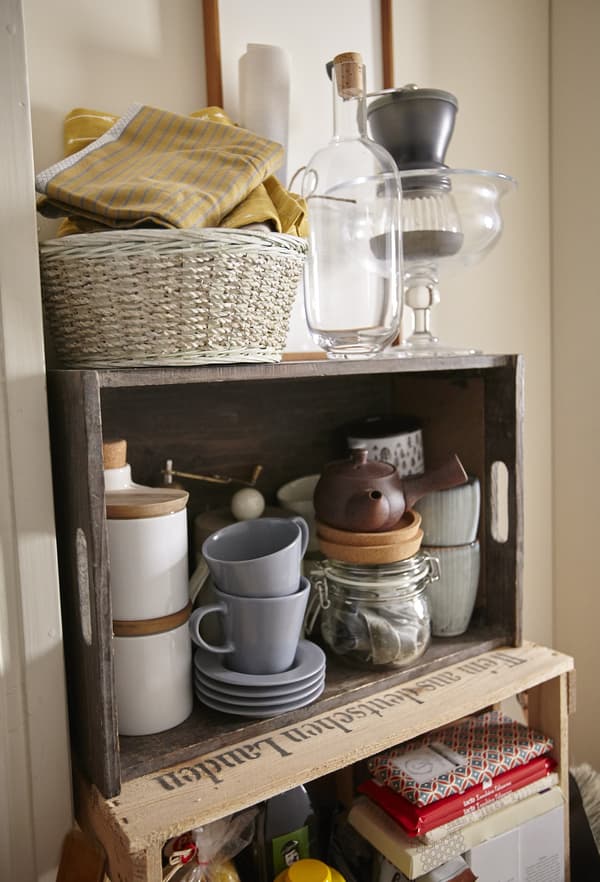 Des mugs et de la vaisselle dépareillés sont rangés dans un cageot en bois pour un effet vintage dans la cuisine.