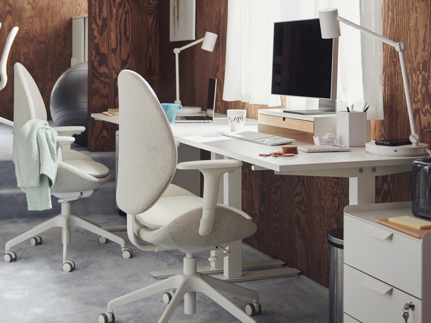 Des postes de travail comprenant des bureaux TROTTEN blancs et des chaises de bureau HATTEFJÄLL et LÅNGFJÄLL, dans un bureau avec du tapis et des murs de lambris brun.