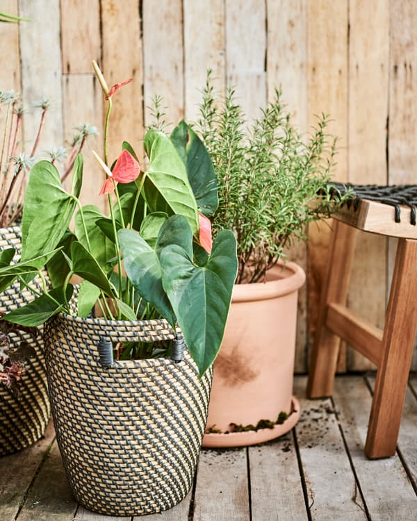 Des pots en terre cuite et en fibres naturelles sur une terrasse en bois, à côté d’un tabouret en bois avec une assise en corde noire.