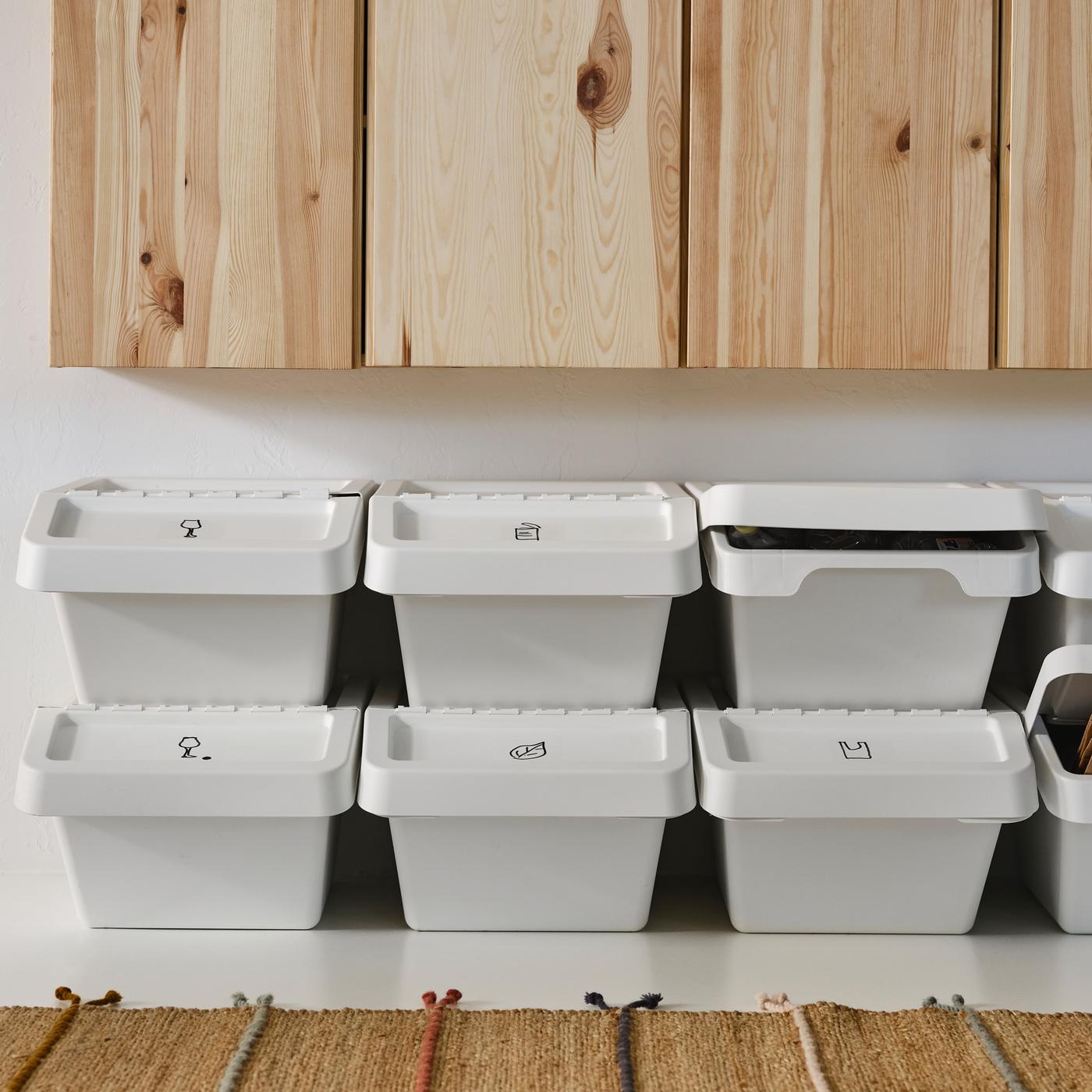 Des rangées de poubelles avec couvercle SORTERA blanches empilées sous des armoires en pin, accompagnées d’un tapis.