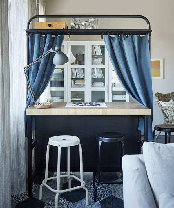 Des rideaux bleus suspendus au support d’un îlot de cuisine avec des tabourets de bar RÅSKOG installés en face.