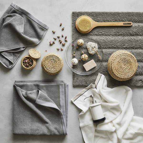 Des serviettes grises et des accessoires de salle de bain déposés sur une surface grise.