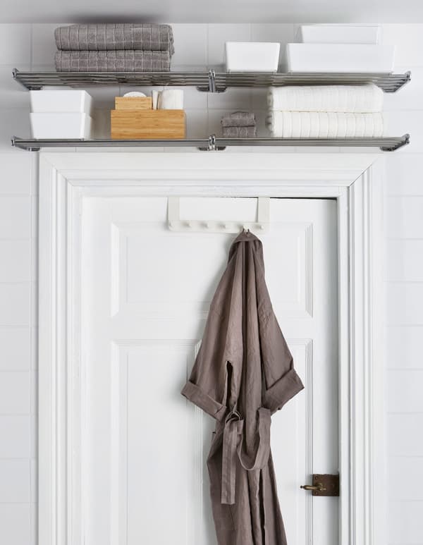 Des tablettes métalliques installées au-dessus du cadre de la porte servent de rangement aux serviettes et autres. Un peignoir est accroché à une patère pour porte.