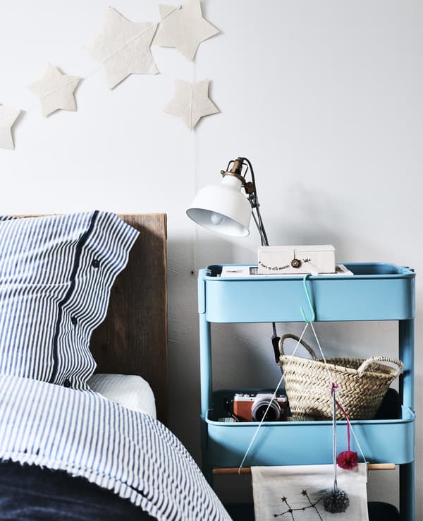 Desserte bleue utilisée comme table de chevet, avec lampe posée dessus.