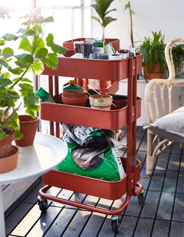 Desserte rouge remplie d’accessoires de jardinage et de plantes.