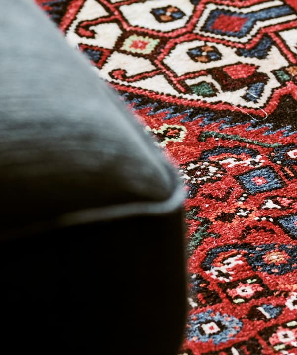Detail of a Persian rug woven into a pattern with blue and green shapes on a red background.