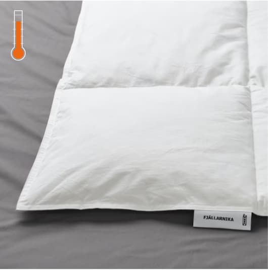 Detalle de una cama, se muestra en primer plano un edredón FJÄLLARNIKA y en la esquina superior izquierda un termométro ''cálido''''.