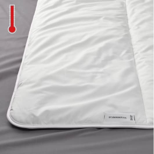 Detalle de una cama, se muestra en primer plano un edredón STJÄRNBRÄCKA y en la esquina superior izquierda un termométro ''caliente''.
