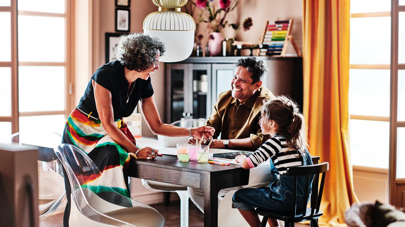 Deux adultes et un enfant autour d’une table à rallonge EKEDALEN brun foncé. L’enfant est assis sur une chaise junior AGAM.