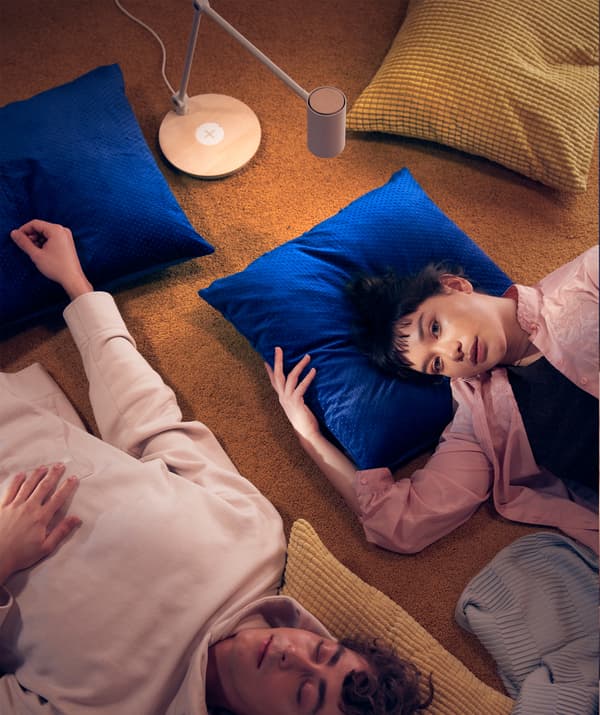 Deux amis allongés sur le sol, la tête reposant sur des coussins.