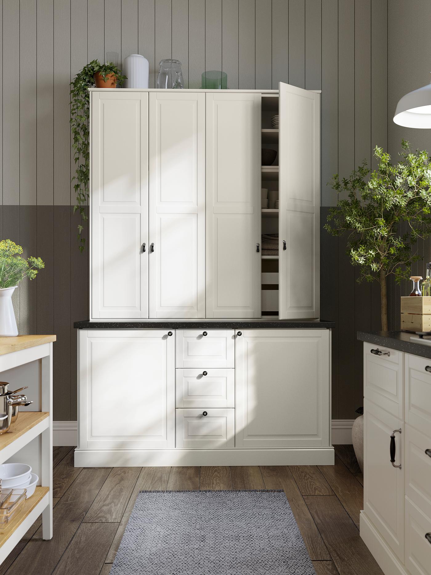 Deux armoires avec des portes blanc cassé, l’une des portes est ouverte laissant apparaître les tablettes à l’intérieur. Plus bas, d’autres armoires avec des façades de tiroirs blanc cassé.