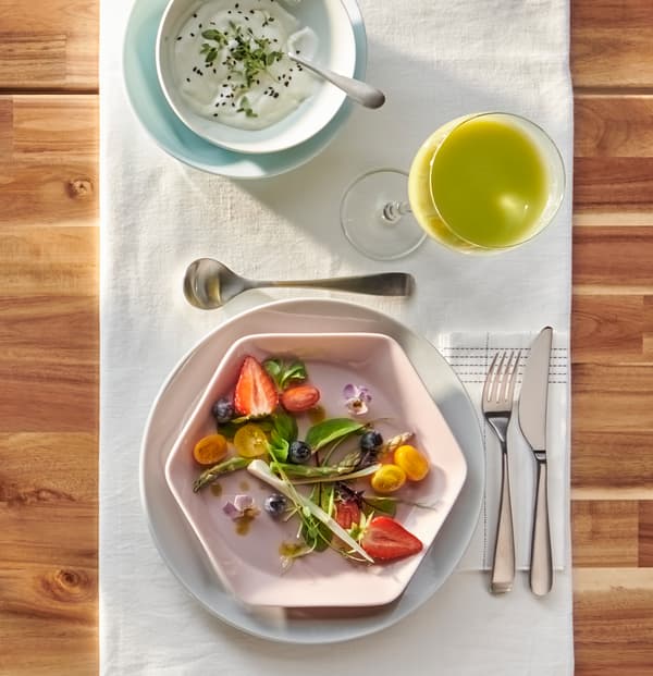 Deux assiettes rondes grises et bleu clair, bol blanc et assiette hexagonale rose FORMIDABEL avec salade estivale.