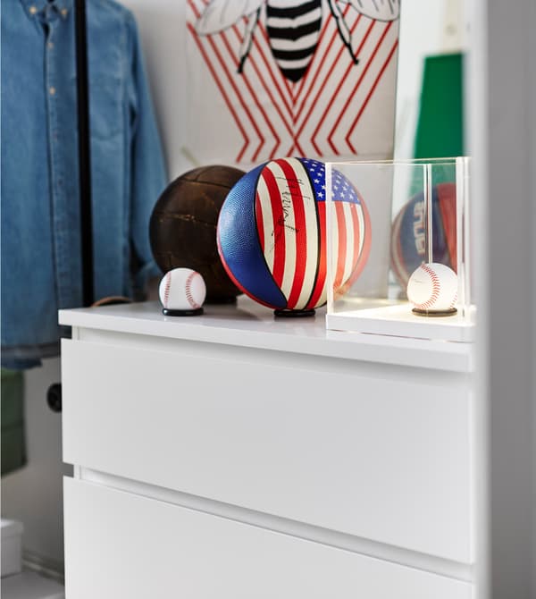 Deux balles de base-ball et des balles de basket posées sur une commode blanche.