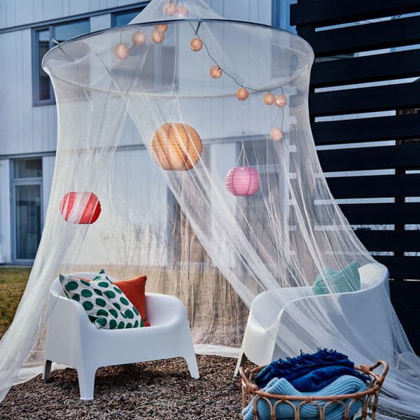 Deux chaises en plastique à l’intérieur d’une moustiquaire suspendue ornée de guirlandes lumineuses et de lanternes.