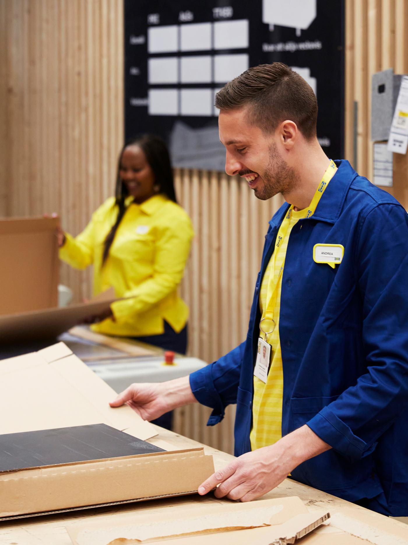 Deux collaborateurs IKEA, l’un vêtu d’une veste bleue et l’autre d’une veste jaune, qui emballent des articles dans un emballage de carton.