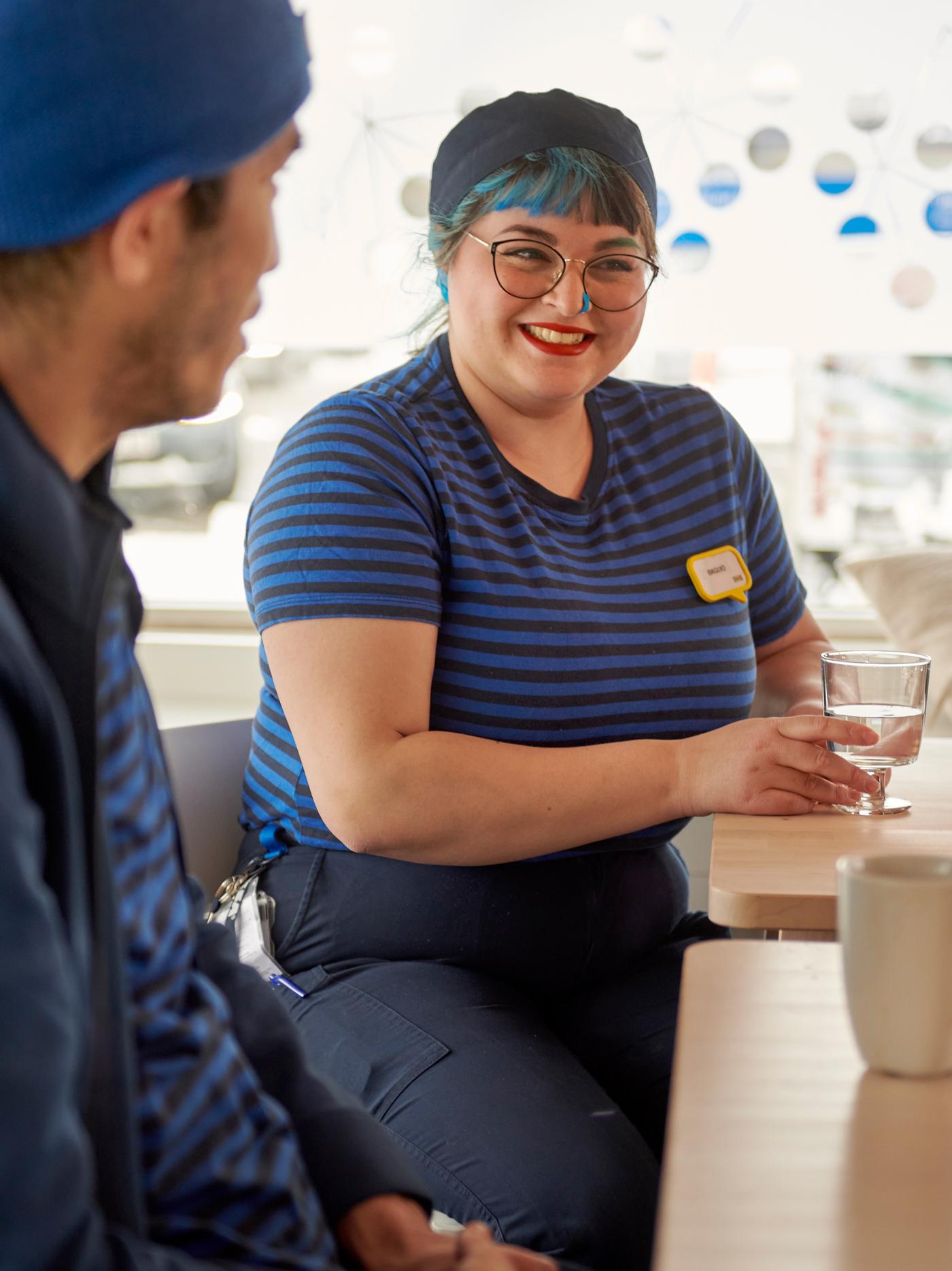 Deux collaborateurs IKEA, l’une aux cheveux bleus, qui prennent un verre d’eau à la cantine du personnel.