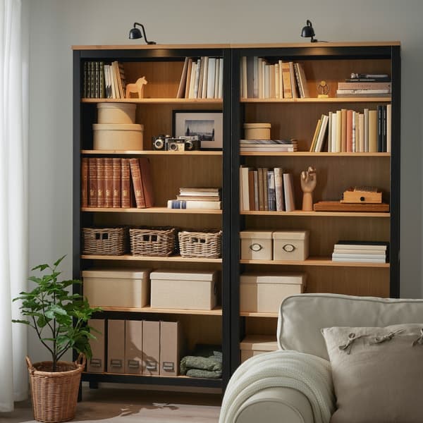 Deux étagères remplies de livres et d’accessoires avec deux spots TVÄRDRAG installés au-dessus des bibliothèques.