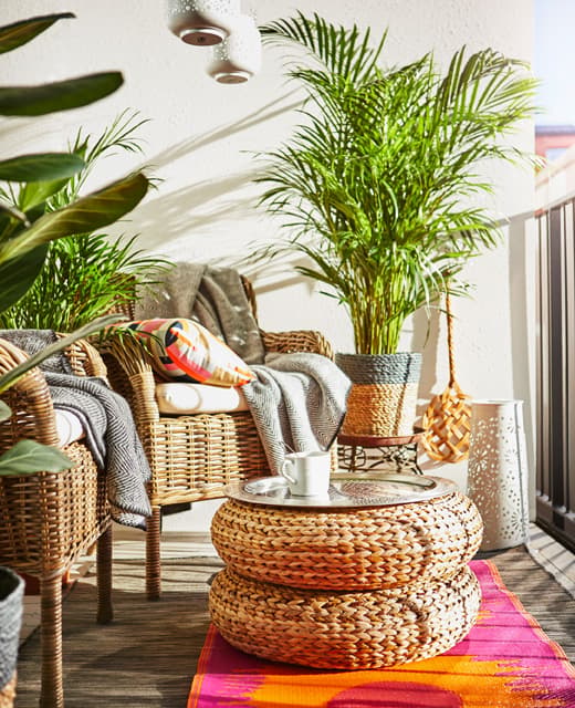 Deux fauteuils en rotin, deux poufs empilés faisant office de table, plantes et tapis aux couleurs vives trouvent place au balcon.