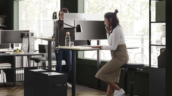 deux femmes travaillent à un bureau debout, à moitié assises sur un tabouret haut
