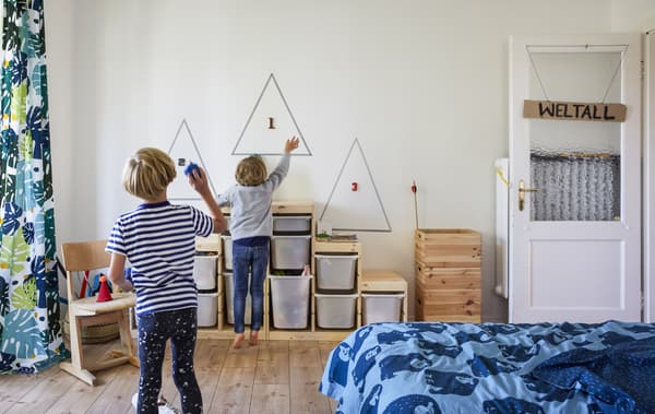Deux garçons en train de jouer dans une chambre avec des rangements pour les jouets contre le mur.