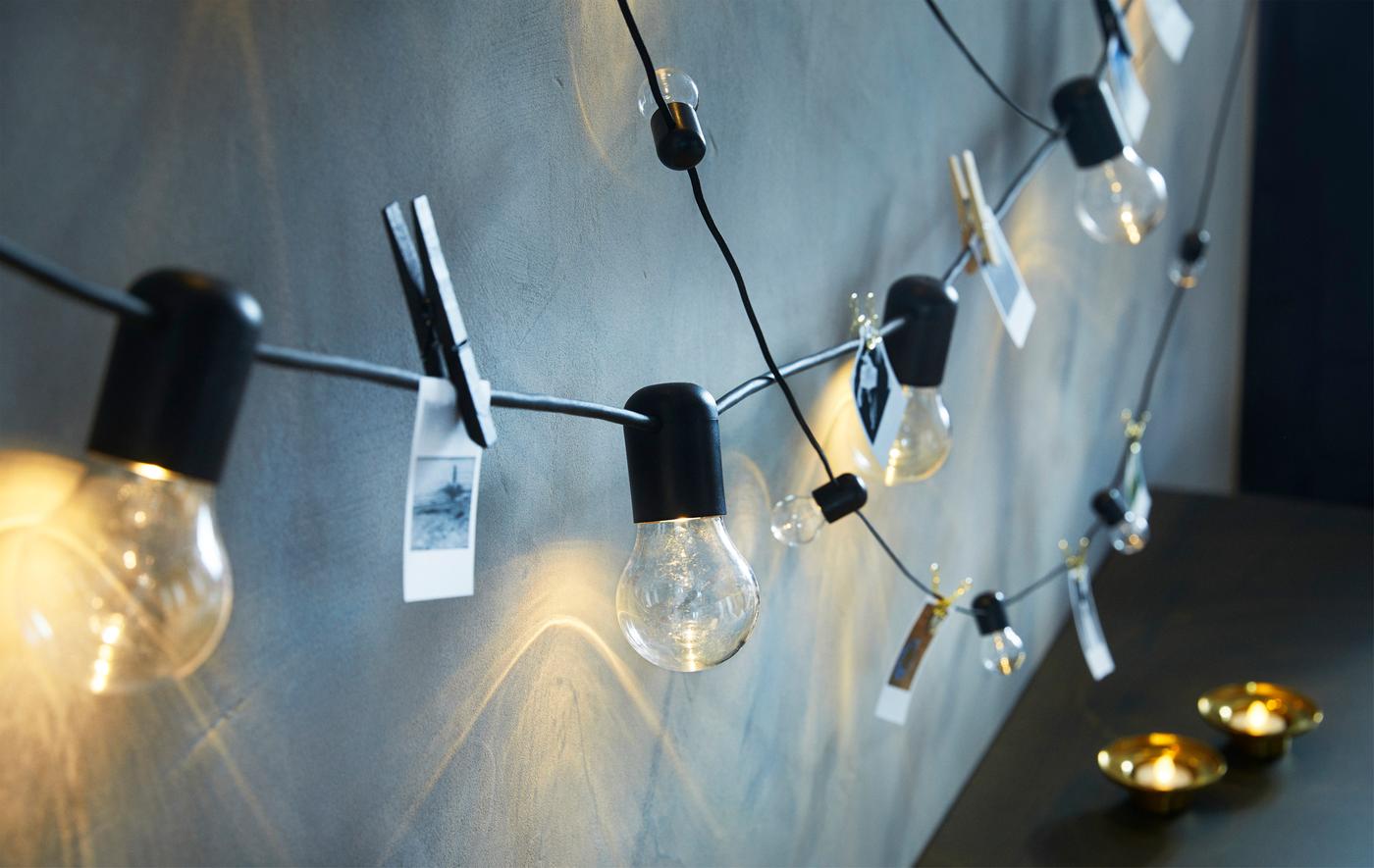 Deux guirlandes lumineuses noires suspendues à un mur avec de petites illustrations accrochées aux cordons entre les ampoules.