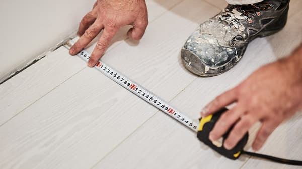 Deux mains tenant un ruban à mesurer sur un plancher en bois blanc.