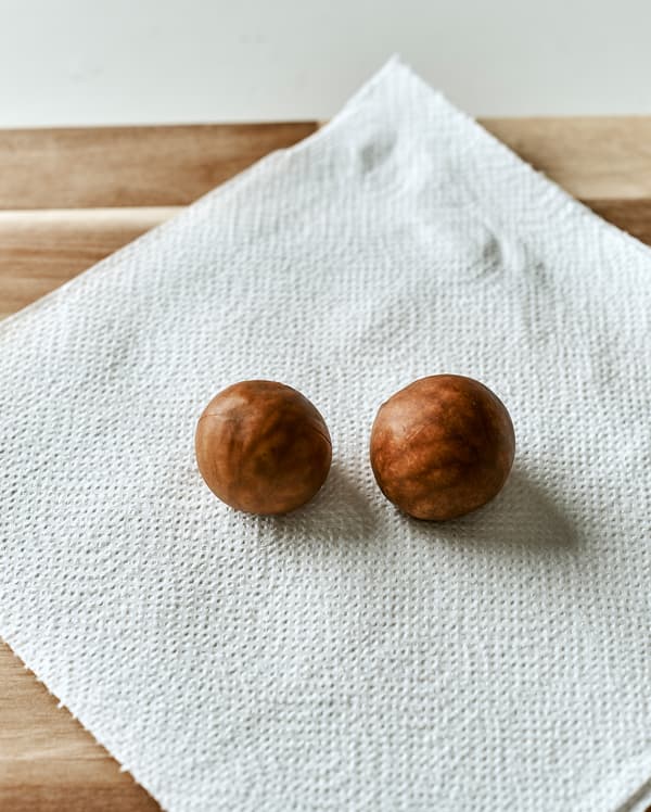 Deux noyaux d’avocat placés sur une feuille d’essuie-tout sur une planche à découper en bois.