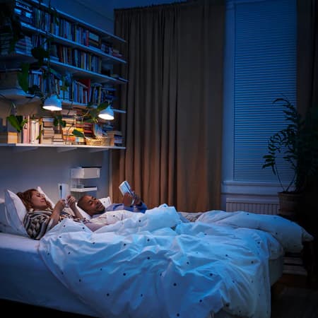 Deux personnes au lit avec quelques lumières encore allumées qui éclairent la pièce sombre.