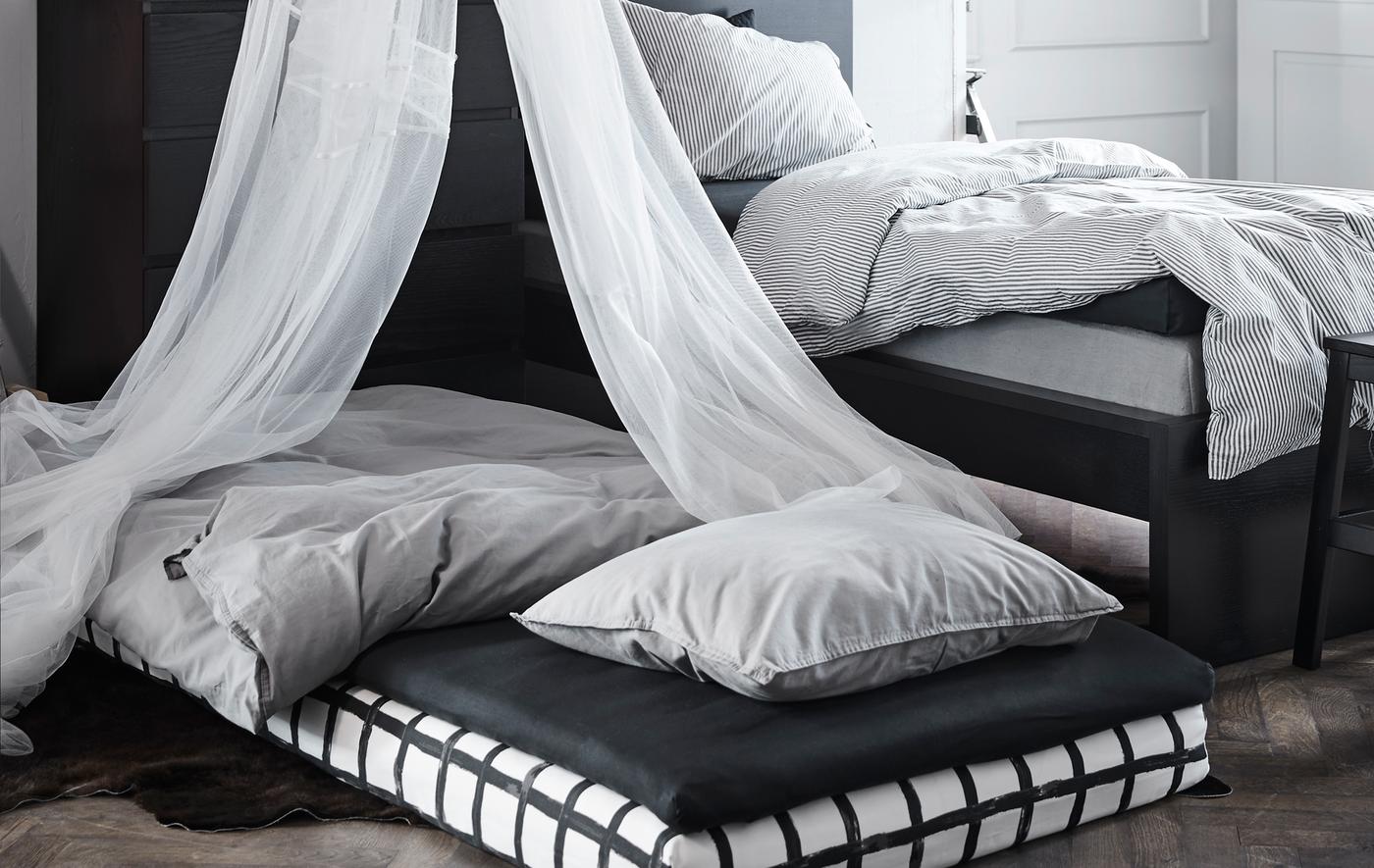 Deux petits matelas empilés et arrangés en lit sur le sol, à côté du lit. Un ciel de lit surplombe le lit d'appoint.