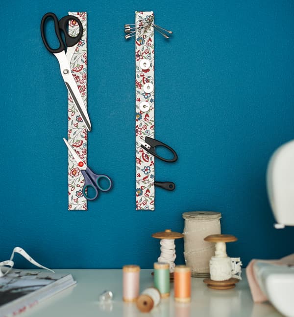 Deux rails à couteaux magnétiques recouverts de tissu à fleurs servent de rangement aux ciseaux et accessoires de couture. 