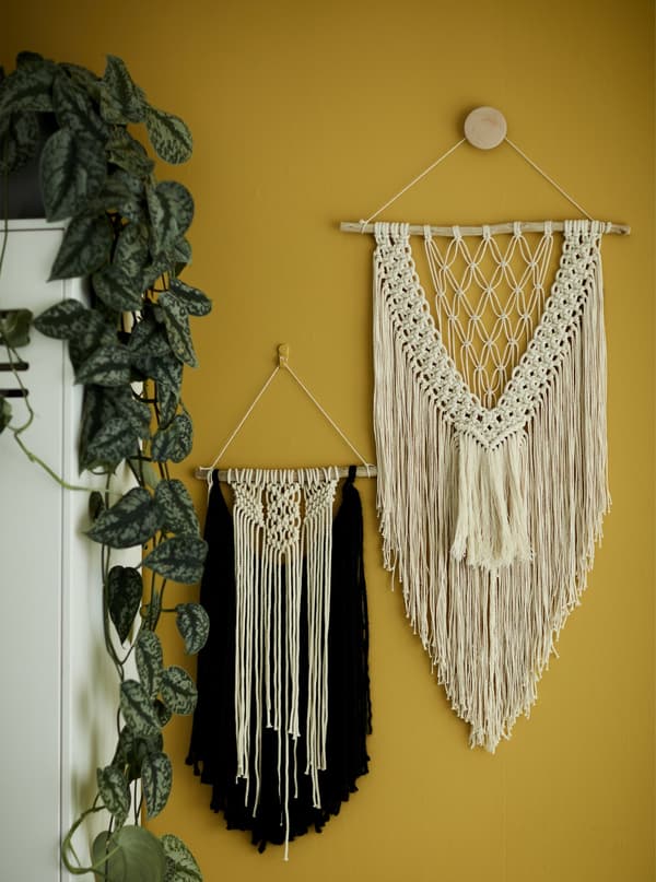 Deux réalisations en macramé accrochées à un mur jaune.