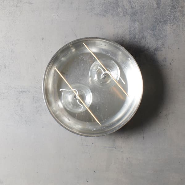 Deux supports en verre avec des mèches flottent dans de l'eau chaude, soutenus par des bâtonnets en bois, comme si un projet de bricolage IKEA était en cours de réalisation au milieu du processus de fabrication de bougies.