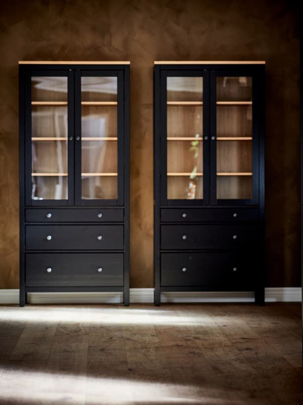 Deux vitrines foncées HEMNES vides appuyées contre le mur brun d’une pièce vide.