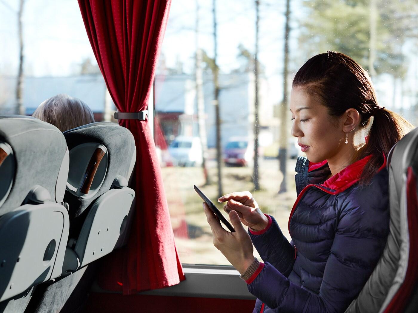 Devojka u autobusu sedi i gleda telefon